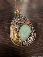 Front view of the vintage pendant necklace showing the teardrop turquoise stone surrounded by intricate mixed metal work in copper, brass, and silver tones.