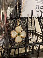 Close-up of the flower pendant showing the gold-toned metal, pearl-like petals and the central green stone on a fishnet display stand.