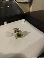Front and angled views of the vintage cat brooch with green jade belly and gem eyes inside a jewelry box.