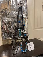 Photo showing the full necklace hung on a decorative Eiffel Tower model, highlighting the size, design, and distribution of turquoise colored stones along the silver-toned chain.