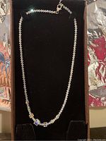 Photo of Swarovski crystal necklace displayed flat on black velvet background, showing faceted clear crystals and cube-shaped crystals near center.
