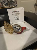 Front angled view of the Swarovski peacock brooch showing large clear crystal body and gold-tone tail with smaller crystals, red enamel head and blue eye crystal.