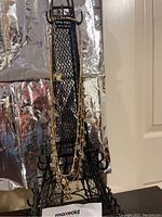 Vintage Anne Klein necklace displayed hanging on an Eiffel Tower shaped stand with a metallic reflective background, showing the full length and design of the necklace.