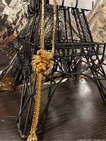 Front view of gold electroplated lion head pendant necklace hanging on a black miniature Eiffel Tower structure.