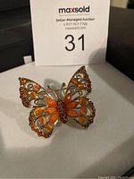 Photo of vintage butterfly brooch showing full front detail with colorful orange and amber stones on filigree gold-tone metal wings.