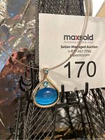 Front close-up of vintage pendant necklace showing silver-tone teardrop pendant with blue oval stone and small round blue gem above it.