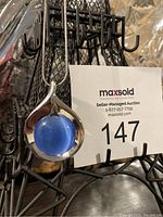 Front view of vintage silver-toned necklace with round blue cat's eye stone pendant on a thin chain, hanging on a display.