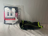 Back brace in clear packaging shown with instruction card alongside the unwrapped knee brace with black and green design.