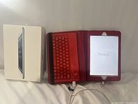 Photo showing the Apple iPad Mini MD532LL/A tablet with the red keyboard case and charging cable, including the original box on the side.