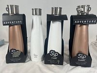 Front view of four Sip by S'well tumblers, two rose gold metallic and two white, each with black labels.