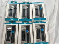Six black Apple Watch bands in original packaging, arranged in two rows of three, showing front view of each packet.