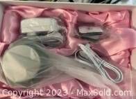 Photo showing cellulite treatment device, power adapter, cords, and cellulite cream wrapped and arranged in pink satin box.