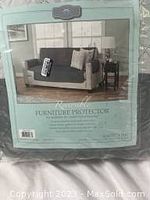 Image of the sofa protector packaging showing a sofa covered with a dark colored protector in a living room setting with pillows and a side table.