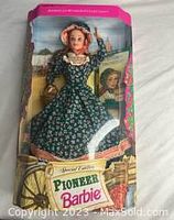 Front view of Pioneer Barbie doll in original box showing doll in green floral pioneer dress and bonnet, with packaging graphics including Barbie logo and American Stories theme.