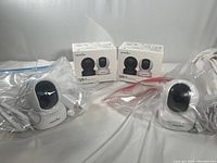 Two Wansview Q5 security cameras in plastic bags with boxes behind on white cloth.
