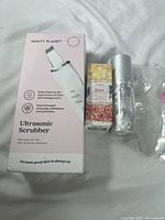 Photo of Vanity Planet Ultrasonic Scrubber box, Yurrku Eden Eye Cream box, and Stages of Beauty Neck Cream bottle in plastic wrap on light fabric background.