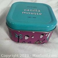 Close-up photo of a square metal candle tin with turquoise lid and purple body decorated with strawberries and hearts, labeled 'Vanilla mousse 6 oz 170 g'.