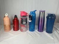Six water and shaker bottles lined up including aluminum, stainless steel, plastic, and BlenderBottle shaker types.