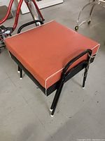 Orange vinyl cushioned stool showing seat and frame detail
