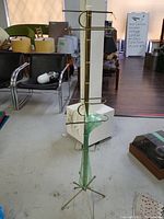 Full view of the vintage atomic era metal hanging rack with brass finish and green glass centerpiece, showing height and base legs.