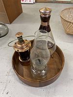 View from above showing two vintage oil lamps, a glass bottle with copper trim and the wooden tray underneath.