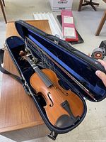 Violin inside open case showing body, fingerboard, tailpiece, chinrest, bow and loose strings