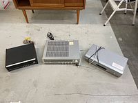 Top down view of the three devices on the floor: black Heathkit tuner with orange knob, silver Yamaha receiver with multiple knobs, silver Sony video player with buttons.