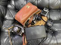 Full view of the brown leather camera bag and several vintage cameras including Polaroid 101, folding camera, and Ricoh case inside.