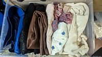 Top-down view of bin with folded leather skirts in blue, black, brown, cream and other clothing.