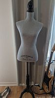 Front view of the gray fabric covered mannequin torso with black wooden stand and printed text 'MADEMOISELLE 1924 Couture de Paris' on front.
