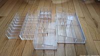 Top-down view of all five clear acrylic makeup organizers showing their compartment layouts and sizes on a wood floor