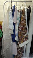 Photo showing a rack with six vintage sleeping gowns and robes in various colors and patterns, hung on metal hangers