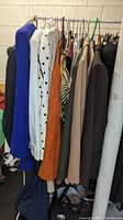 Photo showing multiple women's vintage clothing items hanging on rack in neutral, earth, and bright tones