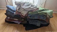 Pile of folded assorted women's clothing including printed skirts, denim, and tops in mixed colors
