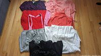 All six women's garments laid on a hardwood floor, showing variety of colors and styles.