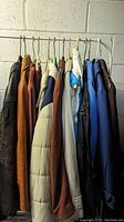 Photo showing a rack of 10 various women's jackets including leather and winter styles in assorted colors hanging on a white metal rack against a cinder block wall.
