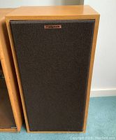 Front of Klipsch Forte speaker with oak veneer cabinet and black cloth grille bearing Klipsch logo