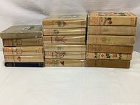 Side view of 17 stacked antique books featuring decorative cloth bindings and some with dust jackets.