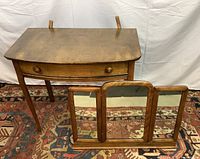 Front view of the antique wooden vanity with the triptych folding mirror detached and in front of it, showing the curved edges, single drawer with two wooden knobs, and tapered legs.