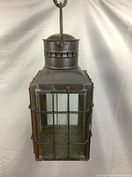 Front view of the rectangular brass lantern showcasing glass windows with protective metal grid and aged brass surface.