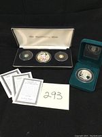 Overview of black display case with three coins, green velvet box with double-headed presidential coin, and certificate cards laid out