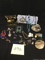 Full overview photo of all jewelry items including rings on a cat holder, necklaces, watch, earrings, and pins laid out on black background