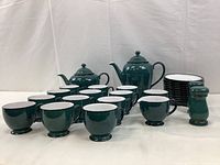 Front angled view of tea set with cups, saucers, pots, and shakers placed on white cloth background