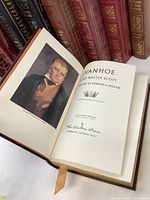 Open book showing 'Ivanhoe' title page with portrait illustration and leather cover with ribbon marker.