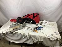 Overview shot of all fencing gear laid out on table including bag, mask, jackets, foils and accessories