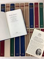 Photo showing front cover and open pages of Mark Twain volume with detailed title and ribbon placeholder, along with aligned slipcases