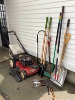 Front view of Toro Recycler lawn mower and garden tools lined against siding