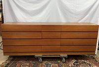 Full front view of the extra long teak dresser showing the entire dresser mounted on a wheeled dolly, illustrating size and drawer fronts
