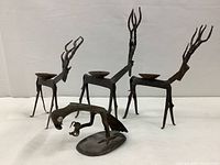 Lot displayed showing two iron deer-shaped candle holders with twisted metal antlers and a brass bird figurine on an oval base in front.