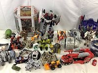 Wide shot showing the arrangement of multiple Transformers action figures, various animal and vehicle forms, and the Jurassic World Nano-Drone in packaging.